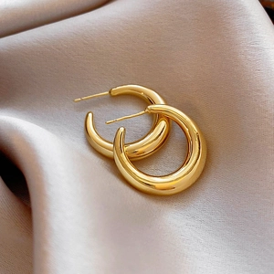 Detailed close-up of polished gold hoop earrings on champagne silk fabric background