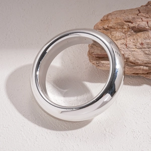 Polished silver geometric round bangle on a minimalist natural background with wood
