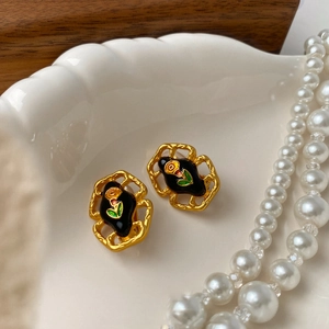 Macro detail of vintage gold plated earrings with black enamel and pearl necklace decor