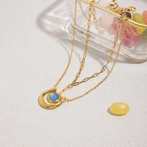 Close-up of double-layer gold necklace featuring blue gemstone horseshoe pendant