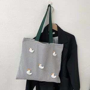 Close-up of striped canvas tote bag with 3D duck dolls and green handles on a hanger