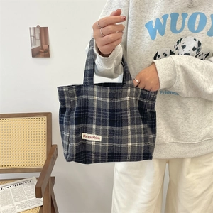 Detail showing blue and grey tartan canvas tote bag with woven brand label detail