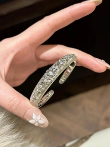 Macro shot of silver open cuff bracelet with hollow floral patterns and zircon inlays
