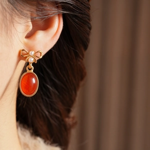 Details von Vintage-Ohrring mit goldener Schleife und rotem Edelstein am Model