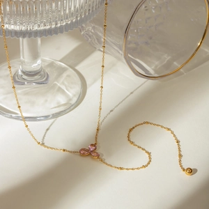 Detail of gold clover necklace featuring three pink gemstones and a delicate bead chain