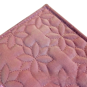 Detail of pink quilted velvet fabric showing petal patterns and fine stitching on the bag