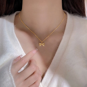 Elegant gold bow pendant necklace on a delicate beaded chain worn by a female model