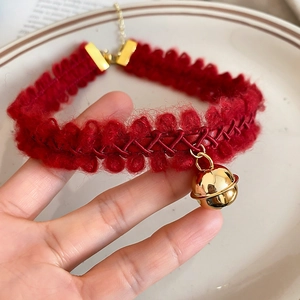 Détail du ras-du-cou en tricot rouge avec pendentif cloche dorée et fermoir ajustable doré