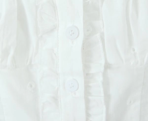 Close-up detail of white lace ruffle top featuring refined buttons and delicate cotton texture