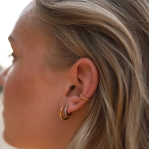 Close-up of gold hoop earrings with blue stones and bead ear cuff on model
