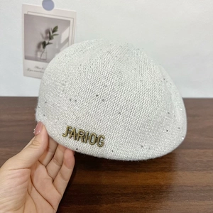 Détail du béret en tricot blanc à paillettes argentées et logo métallique FARIOG