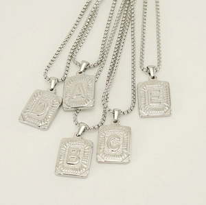 Flat lay of five silver square titanium steel necklaces with A B C D E alphabet pendants