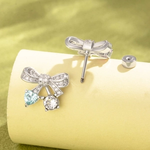 Cute silver bow earrings with light blue heart gems and white round stones on a soft stand