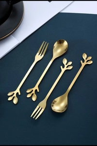 Golden stainless steel cutlery set with elegant leaf-shaped handles on a dark textured mat