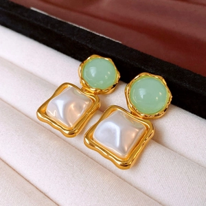 Close-up of geometric resin earrings with green and white pearls in a white jewelry box