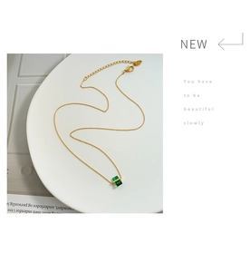 Detail of gold chain necklace featuring a green cubic pendant and a K18 gold tag