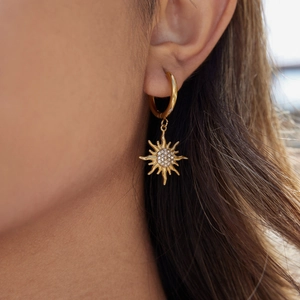 Close-up of a gold sunburst earring with rhinestones on a female model outdoors