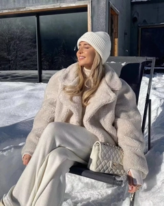 Close-up of beige faux shearling coat worn by a model in a sunny winter snow scene