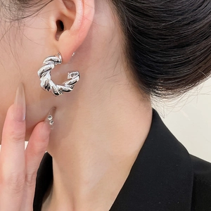 Close-up of a silver twisted C-shaped hoop earring on a model with high polished finish