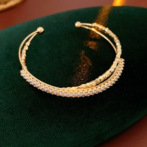 Detailed macro of gold double-layer open bangle with zircons on green velvet