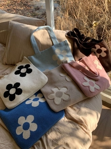 Multiple colorful knitted flower tote bags displayed on a cozy bed in natural sunlight