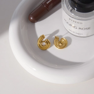Détail macro de boucles d'oreilles spirales dorées avec zircon sur un plateau en céramique