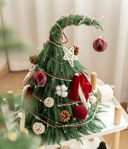 Détail d'un mini sapin de Noël avec nœuds rouges et pommes de pin sur plateau blanc