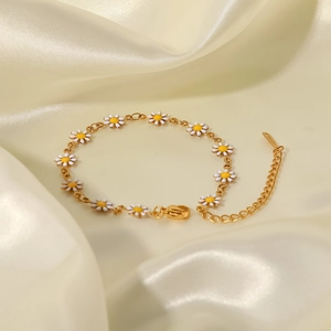Detalle de una pulsera de titanio dorado con margaritas de esmalte blanco sobre seda