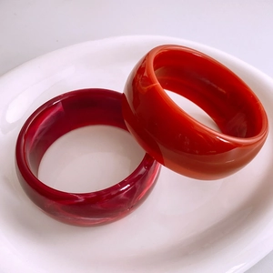 Gros plan de larges bracelets en résine avec motifs sable bordeaux et agate orange