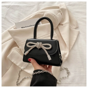 Close-up of a black leather handbag featuring a large sparkling rhinestone bow and chain