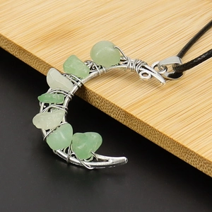 Close-up of crescent moon pendant with green and white crystals on bamboo wood background
