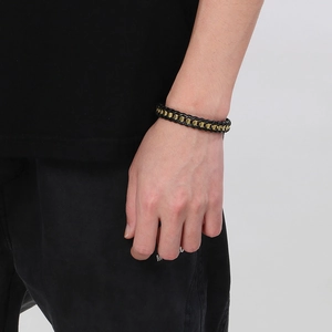 Detailed close-up of men's braided leather bracelet with wavy gold metal accents
