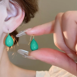 Close-up of vibrant green teardrop earrings with elegant golden hooks on a model