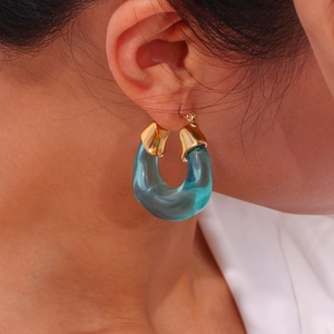 Detail of U-shaped blue resin earring with golden metal clasp on female model