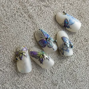 Macro detail of press-on nails featuring 3D purple butterflies and metallic beads