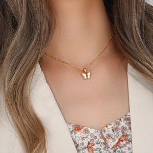 Detailed view of a gold-plated butterfly necklace with white enamel on a model's collarbone