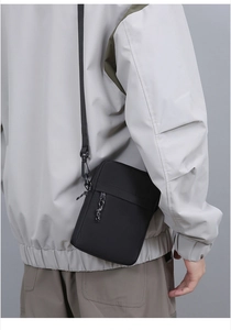 Close-up of a compact black crossbody bag worn over a jacket with adjustable strap detail