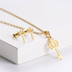 Golden crown key jewelry set including a necklace and earrings on white pedestals