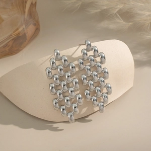 Détail de boucles d'oreilles tressées en maillons argentés sur un support incurvé