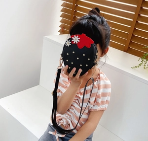 Detail of a black strawberry shaped crossbody bag for girls with gold studs and floral accents