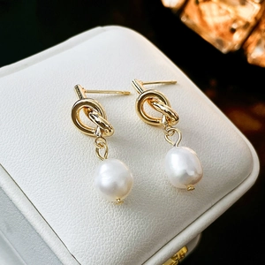 Boucles d'oreilles nœuds dorés et perles d'eau douce sur présentoir en cuir blanc