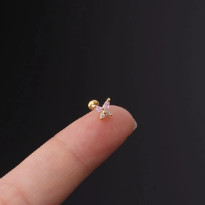 Macro shot of tiny gold butterfly stud earring with pink zircon on a fingertip