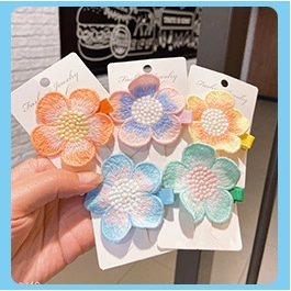 Handheld view of four embroidered floral hair clips in pastel macaron colors with card