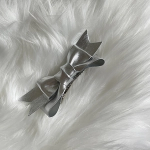 Close-up of a metallic silver bow hair clip on a soft white plush textured background