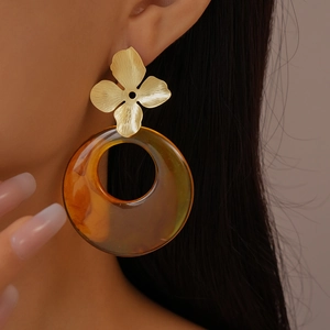Close-up of model wearing gold clover stud with large amber resin hoop earrings