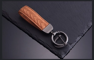 Close-up of brown suede braided leather keychain with gunmetal hardware on a dark base