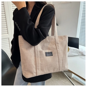 Close-up of beige canvas tote bag with fashion label shown on a female model side profile