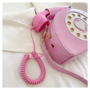 Detail of pink retro telephone shaped crossbody bag featuring glossy patent leather surface