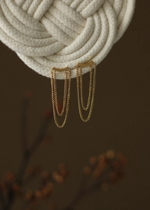 Close-up of elegant gold tassel chain earrings hanging on white woven cotton rope