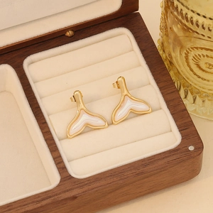 Macro detail of gold whale tail earrings with iridescent pearl inlay in a wooden box